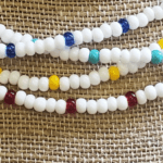 Closeup detail view of white seed bead necklaces with blue, seafoam, yellow, and red accent beads.